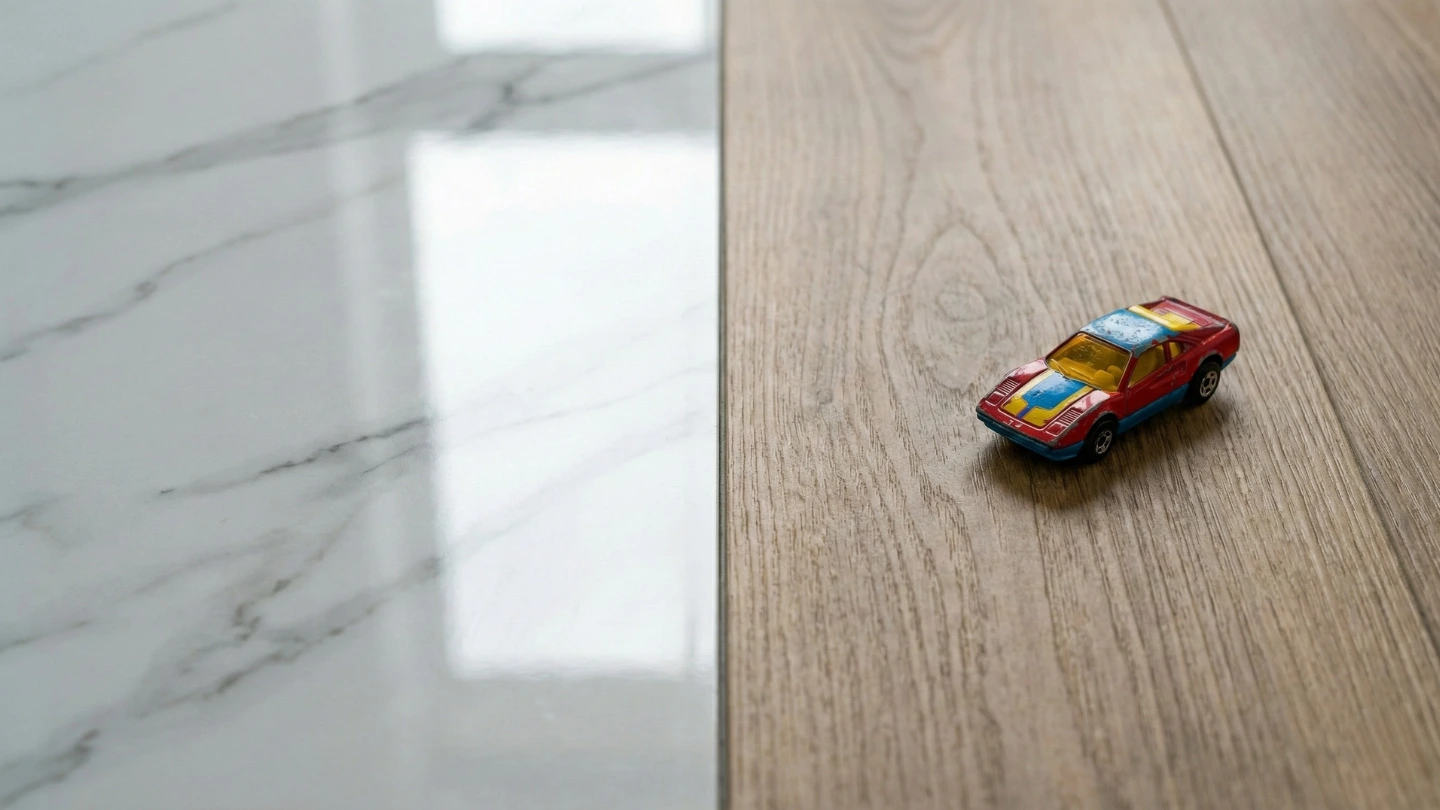 Close-up detail comparing a hard glossy tile against a warm, matte SPC floor plank with a toy car resting on it.