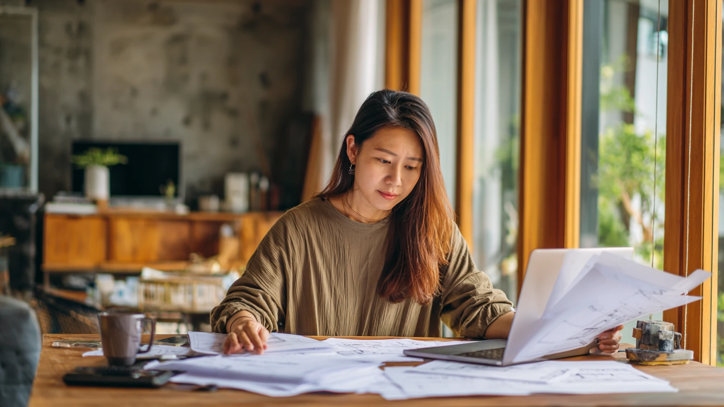 Malaysian homeowner reviewing printed renovation quotation documents at home desk in KL Malaysian homeowner reviewing printed renovation quotation documents at home desk in KL